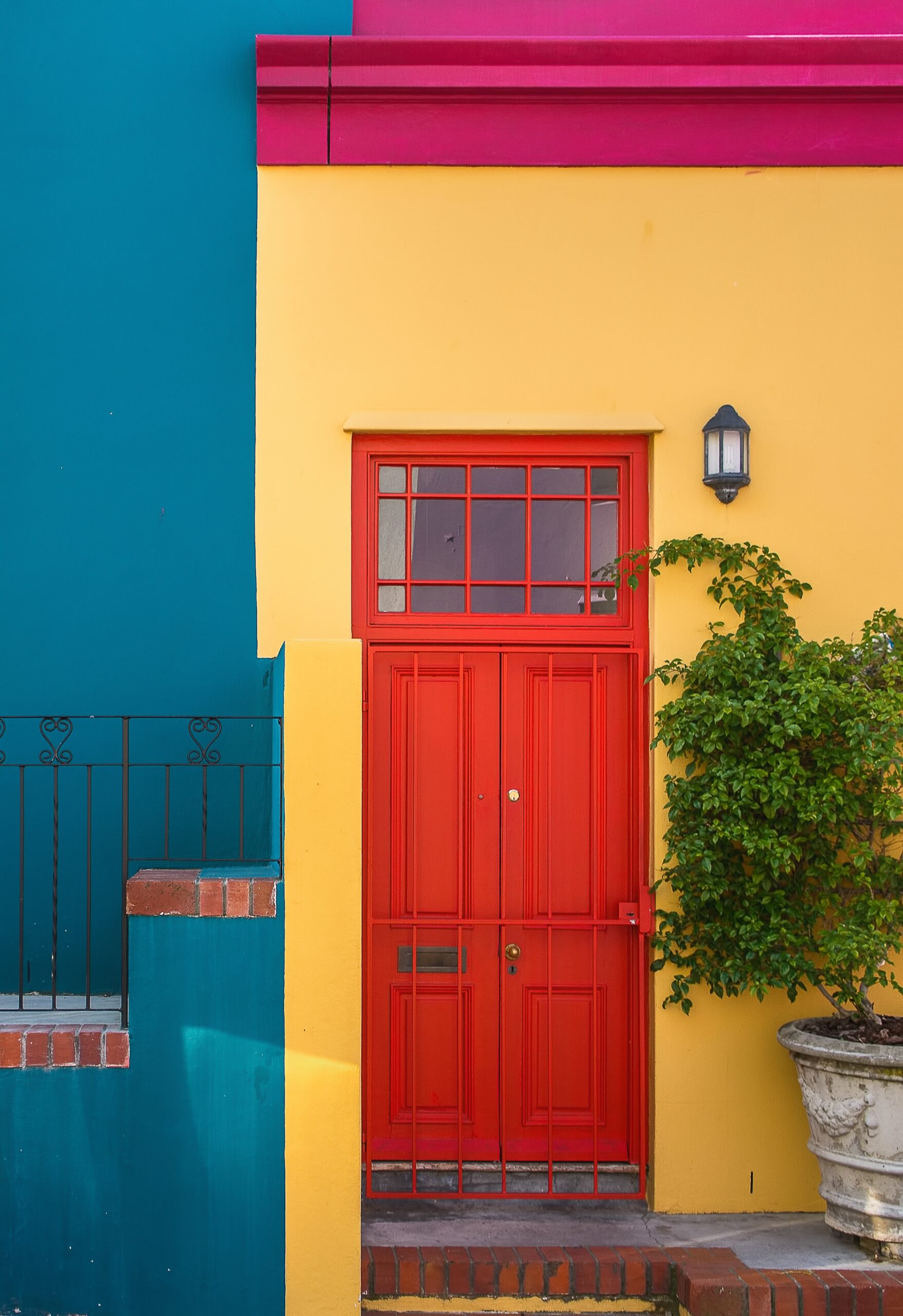 Closeup shot of the red door of a yellow building and a plant next to it