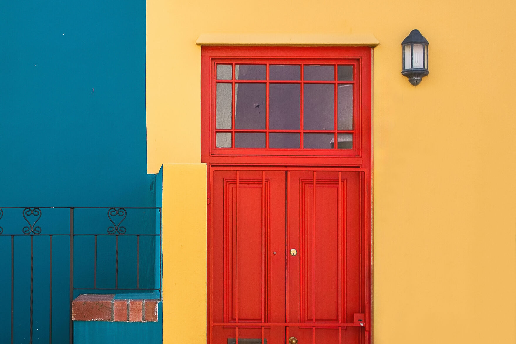 Closeup shot of the red door of a yellow building and a plant next to it Terrae Matera
